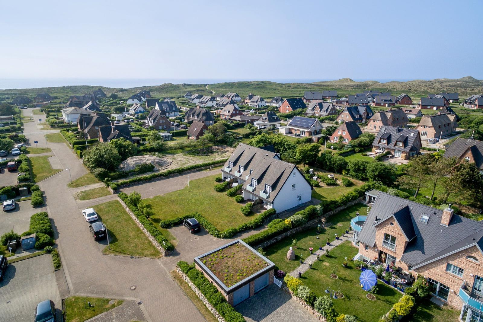 Aerial view of a residential area with houses, green lawns, and distant dunes.
