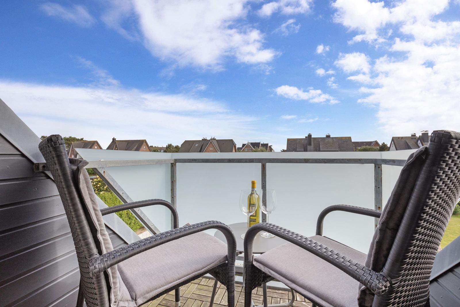 Terrace with two chairs and table, view of rooftops under blue sky.