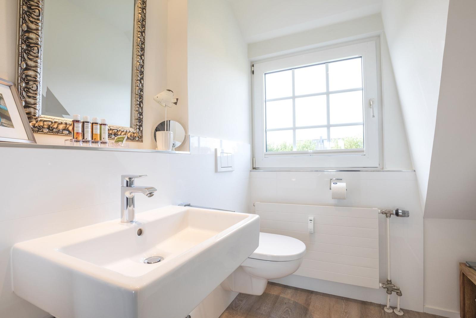 Bathroom with sink, toilet, and window. Mirror with decorative frame.