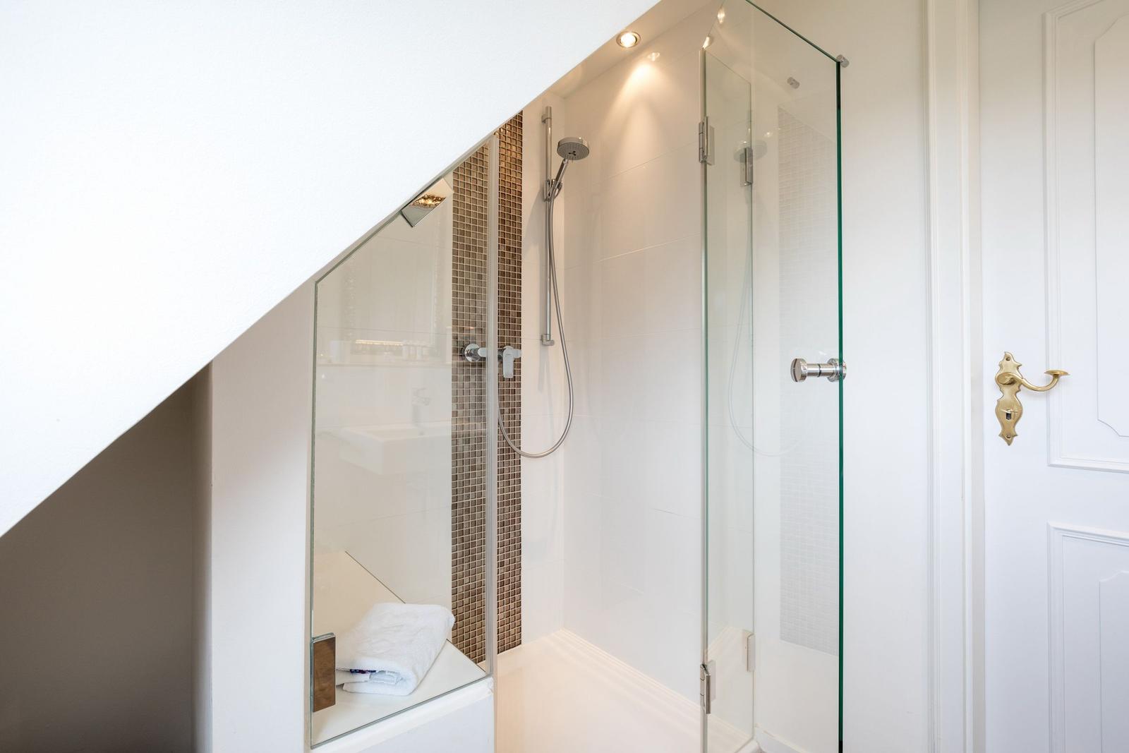 Shower with glass enclosure, brown tiles, and handheld shower