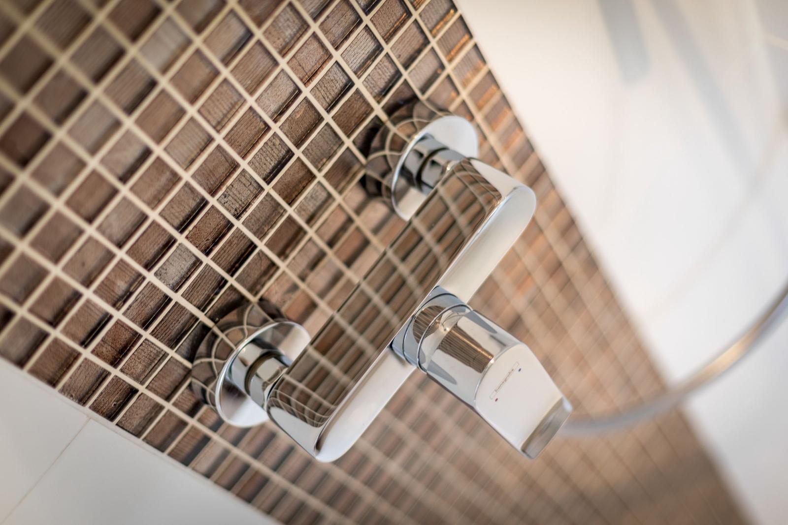 Shower head with chrome faucet on brown tiles
