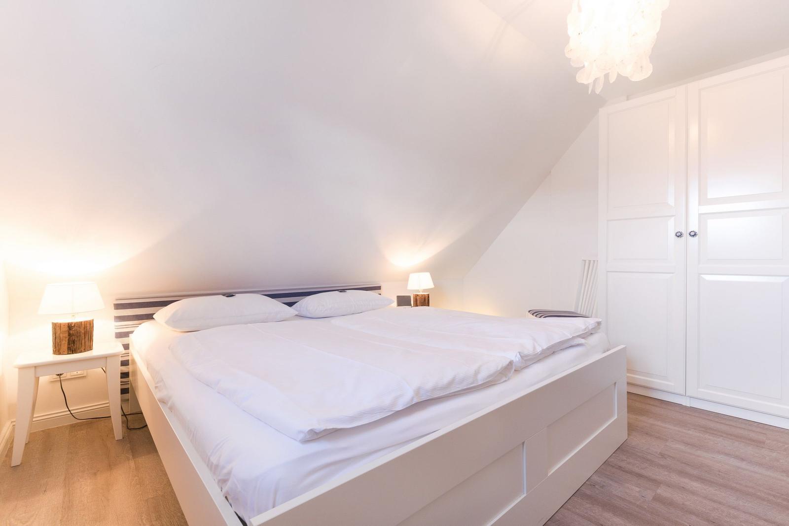 Bedroom with double bed, white nightstands, and a white wardrobe wall.