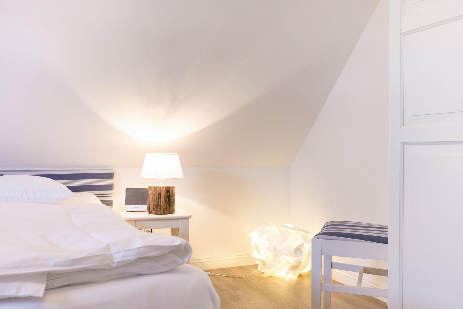 Bedroom with bed, nightstand, lamp, and chair under sloped ceiling.