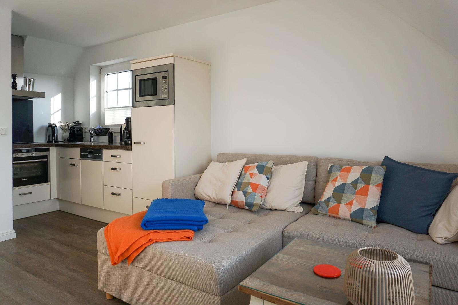 Living room with sofa, cushions, and kitchen area in background.