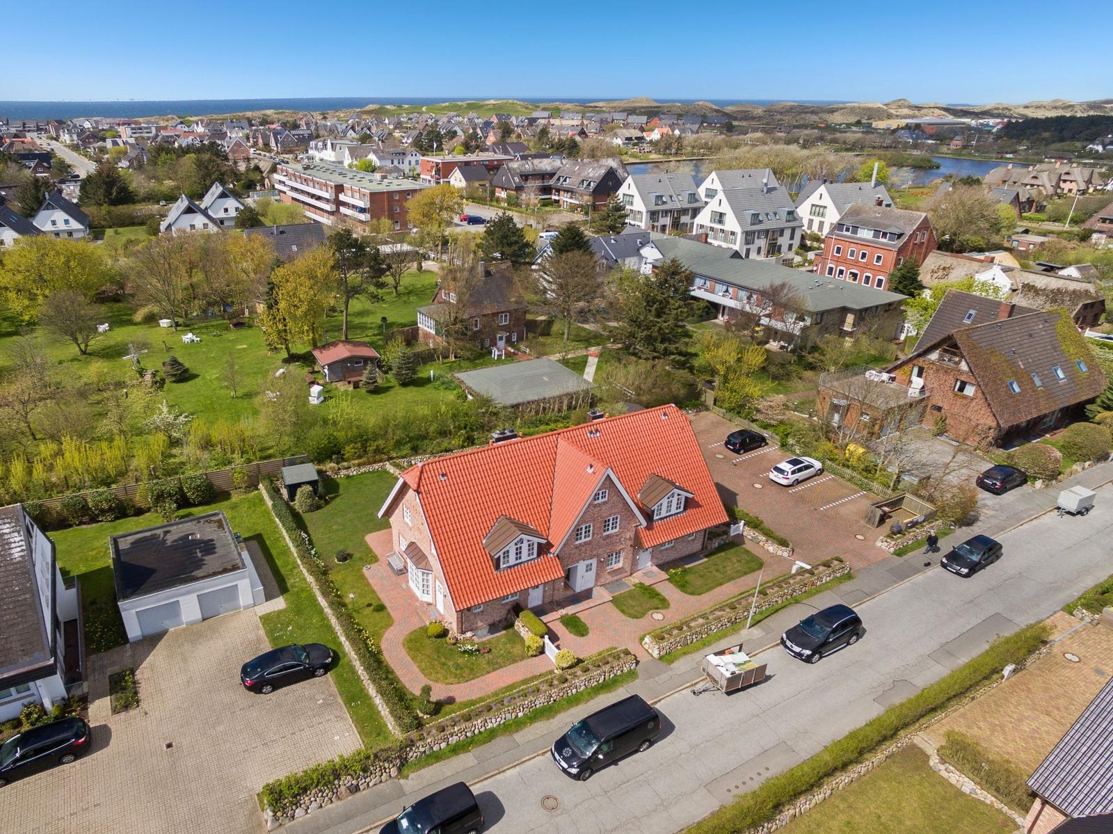 Haus mit rotem Dach, umgeben von Grünflächen und Straßen mit geparkten Autos.