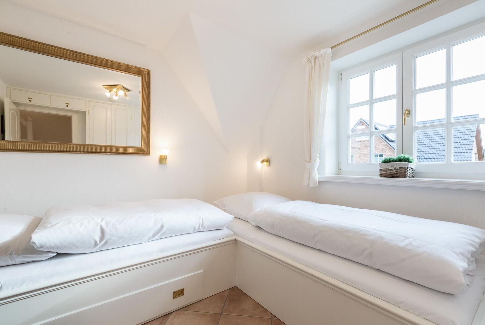 Zimmer mit zwei weißen Betten, Spiegel und Fenster mit Blick nach draußen.