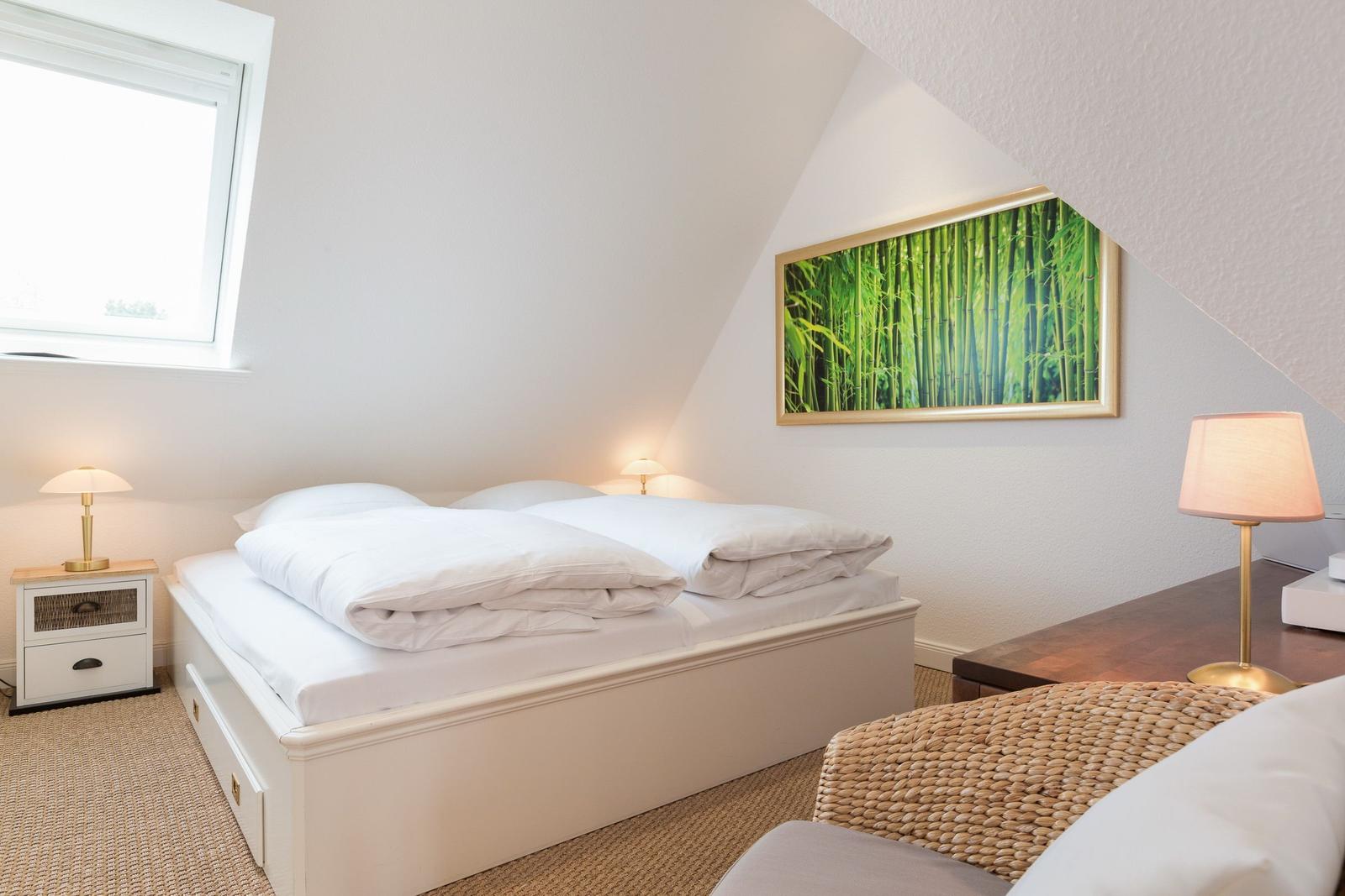 Schlafzimmer mit Doppelbett, Fenster und Wandbild mit Bambusmotiv.
