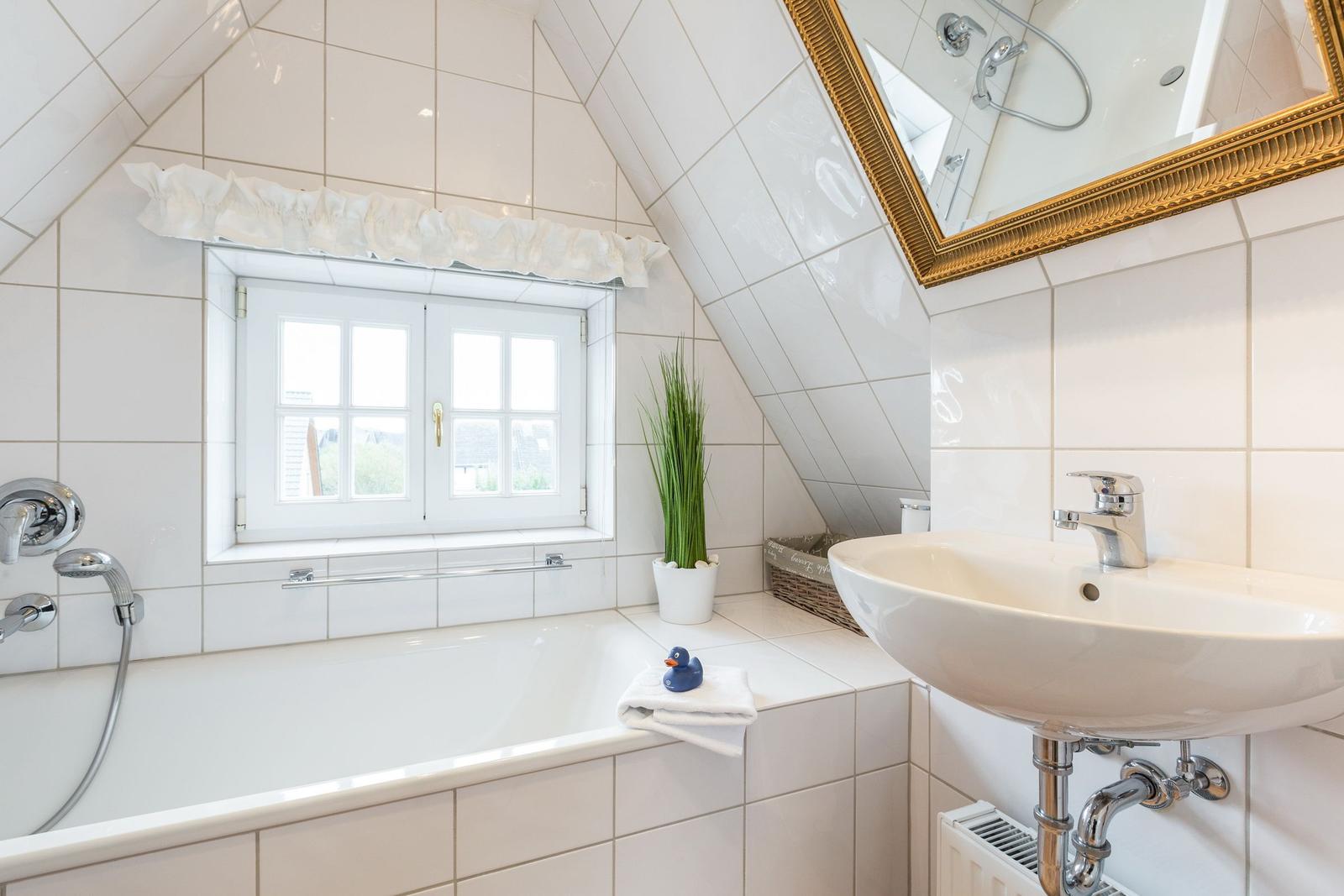 Badezimmer mit Dusche, Waschbecken und Fenster unter Dachschrägen.