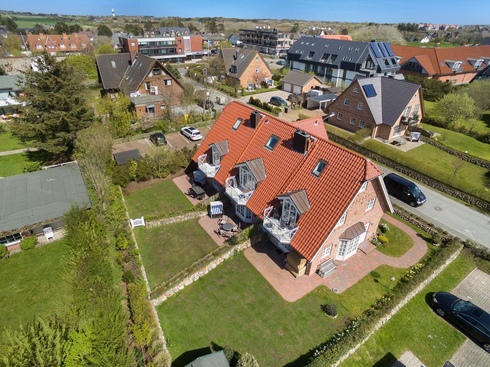Haus mit rotem Dach, Terrasse und Garten. Umgebung mit weiteren Häusern und Grünflächen.
