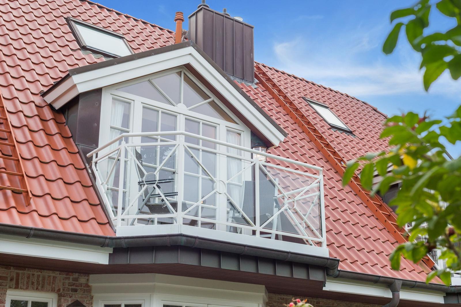 Dachgeschosswohnung mit Balkon und rotem Ziegeldach unter blauem Himmel.