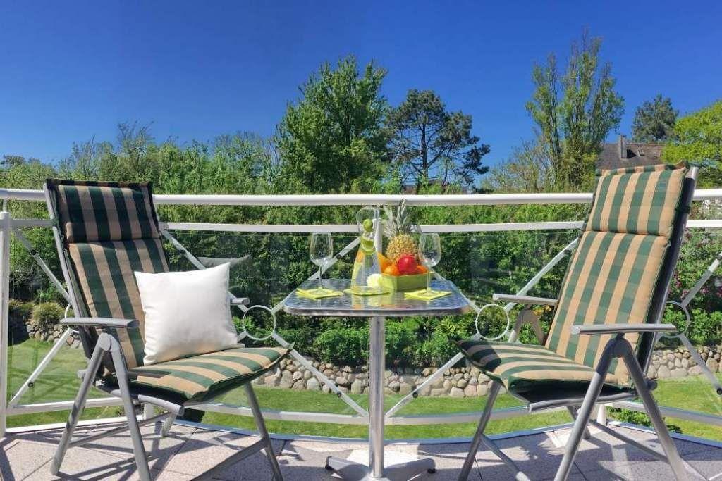 Balcony with two lounge chairs, table, and fruit. Greenery and clear sky in background.