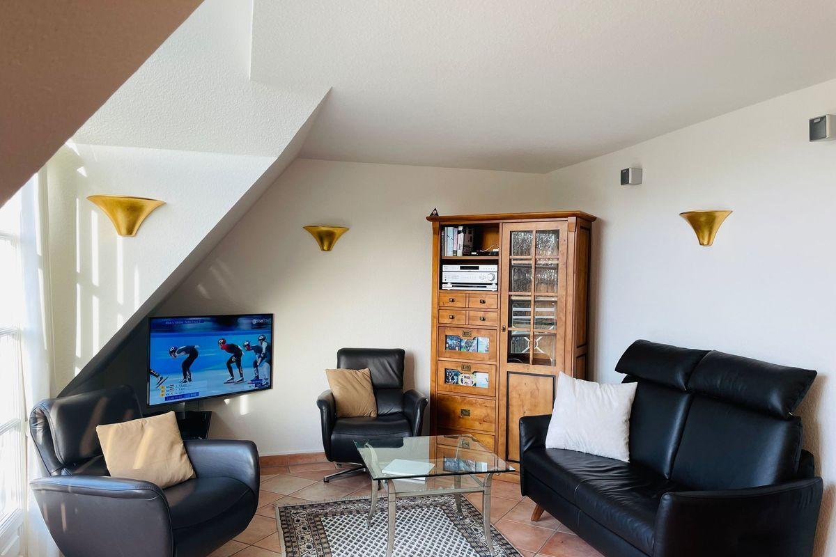 Wohnzimmer mit Sofa, Sessel und Fernseher unter Dachschräge
