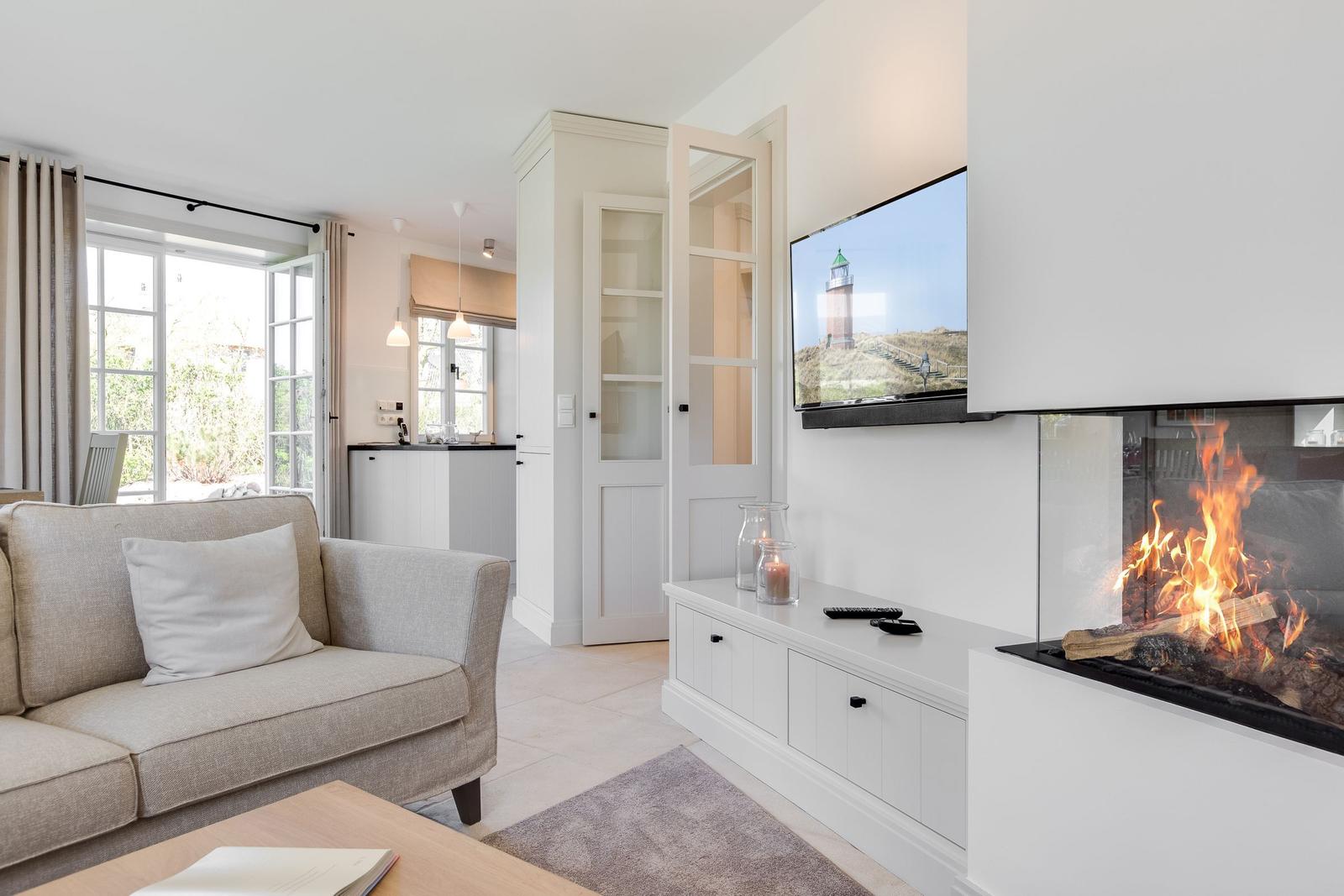 Wohnzimmer mit Sofa, Kamin und Fernseher. Tür führt in die Küche.
