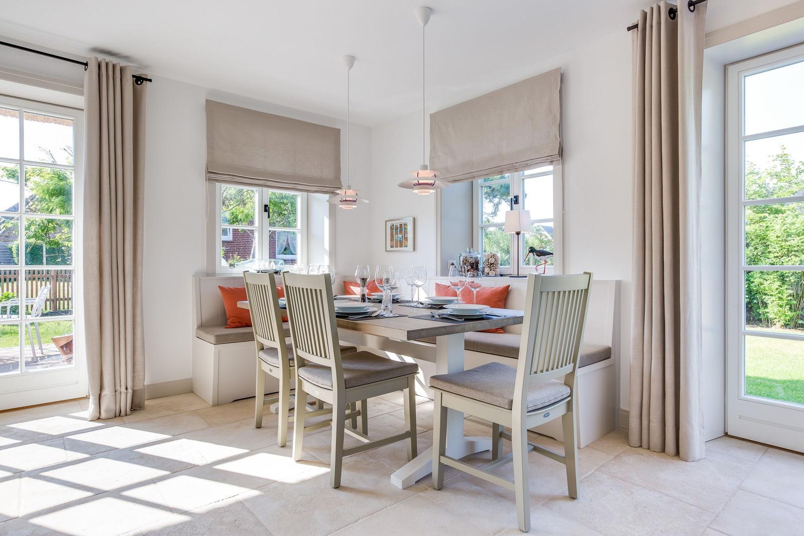 Esszimmer mit Sitzbank, Tisch und Stühlen. Fenster mit Vorhängen und Blick auf Garten.