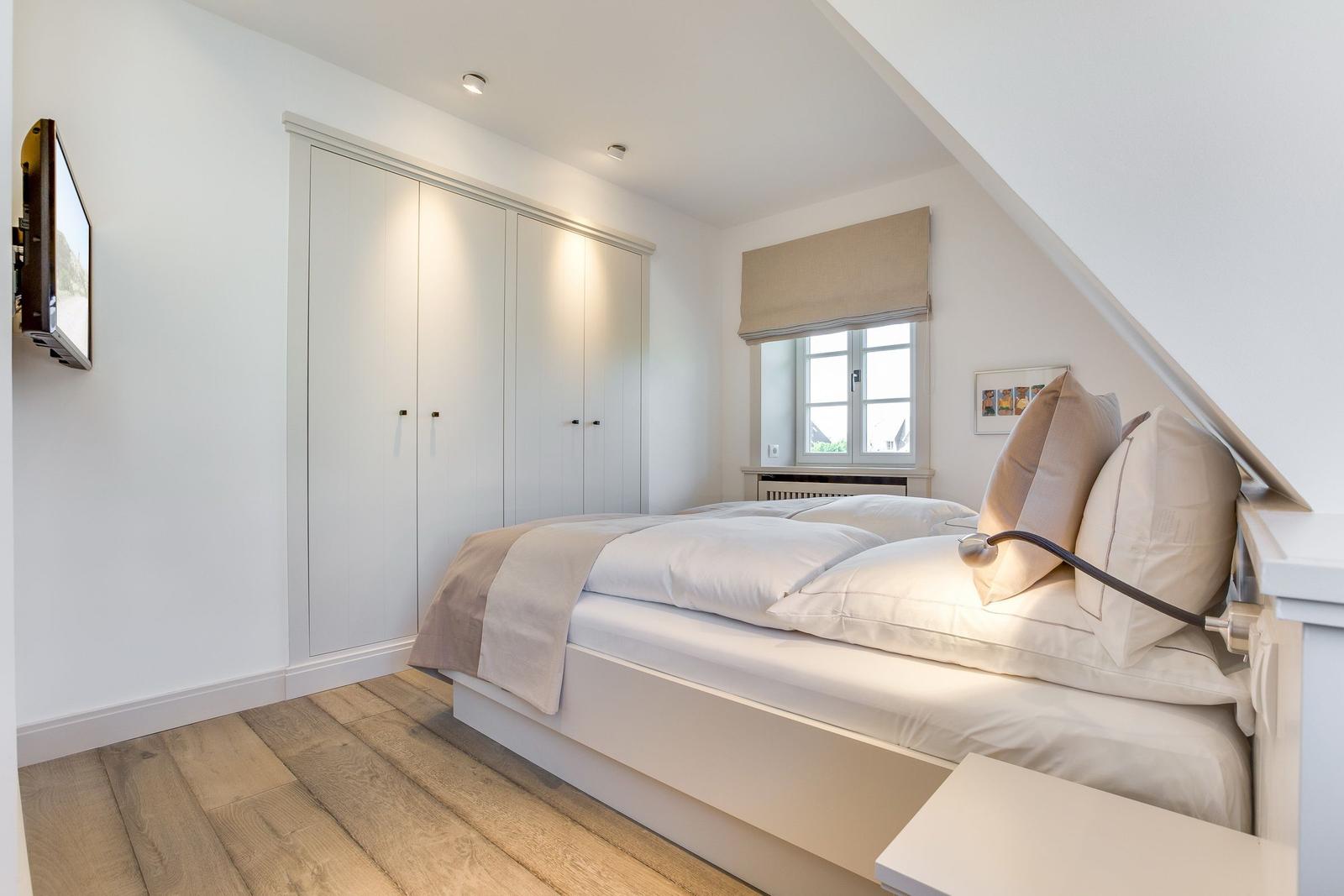 Schlafzimmer mit Doppelbett, Kleiderschrank und Fenster unter Dachschrägen.