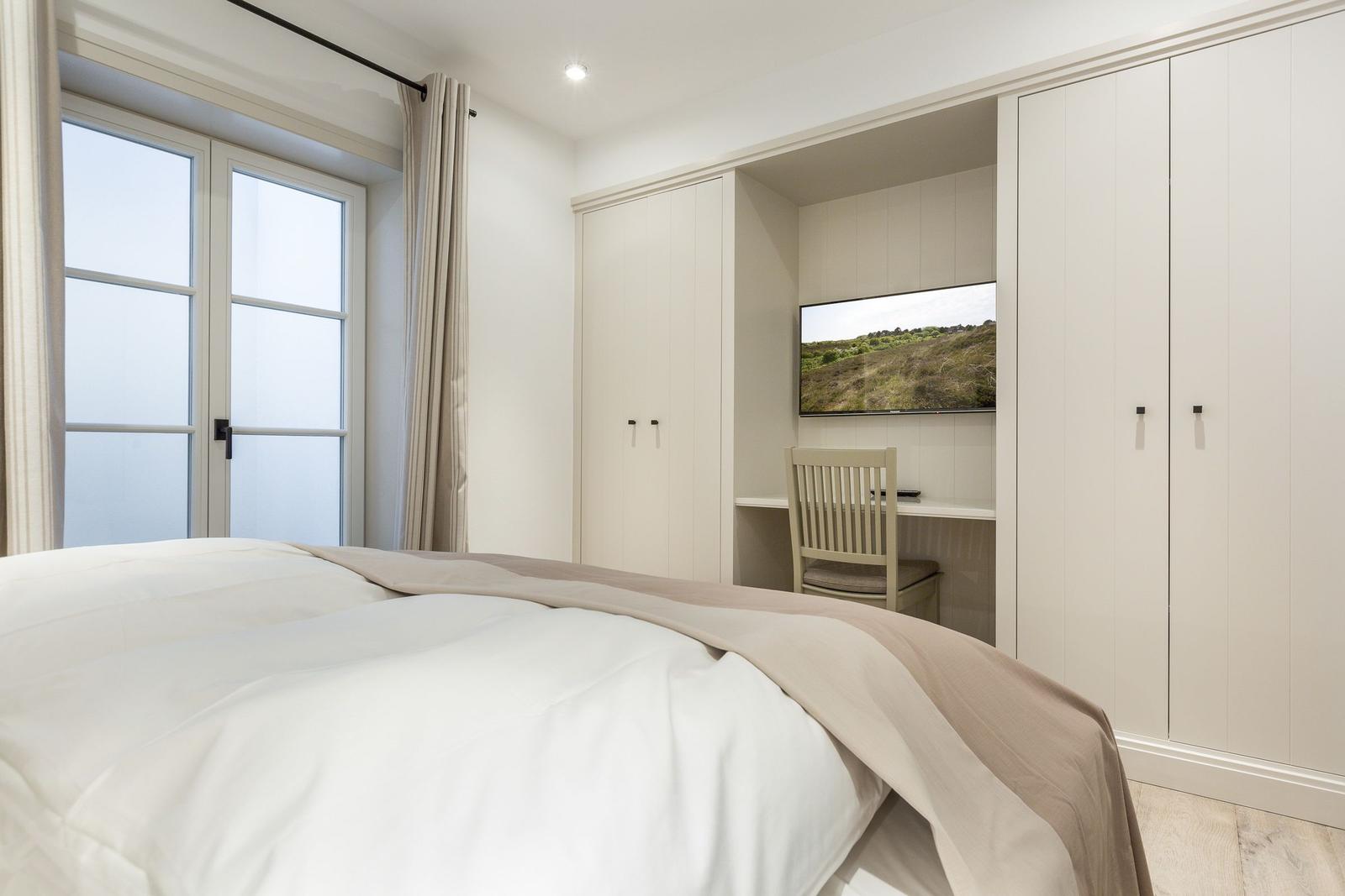 Schlafzimmer mit Bett, Schreibtisch und Fernseher.