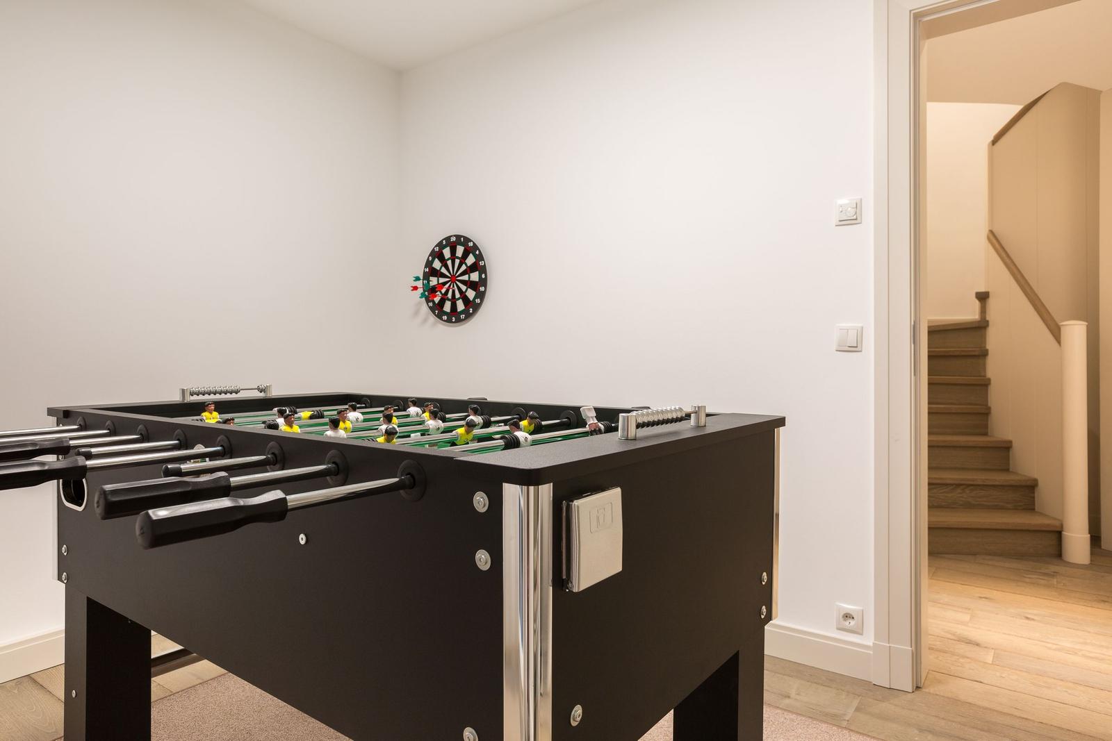 Fussballtisch mit Dartboard an der Wand. Treppenhaus im Hintergrund.