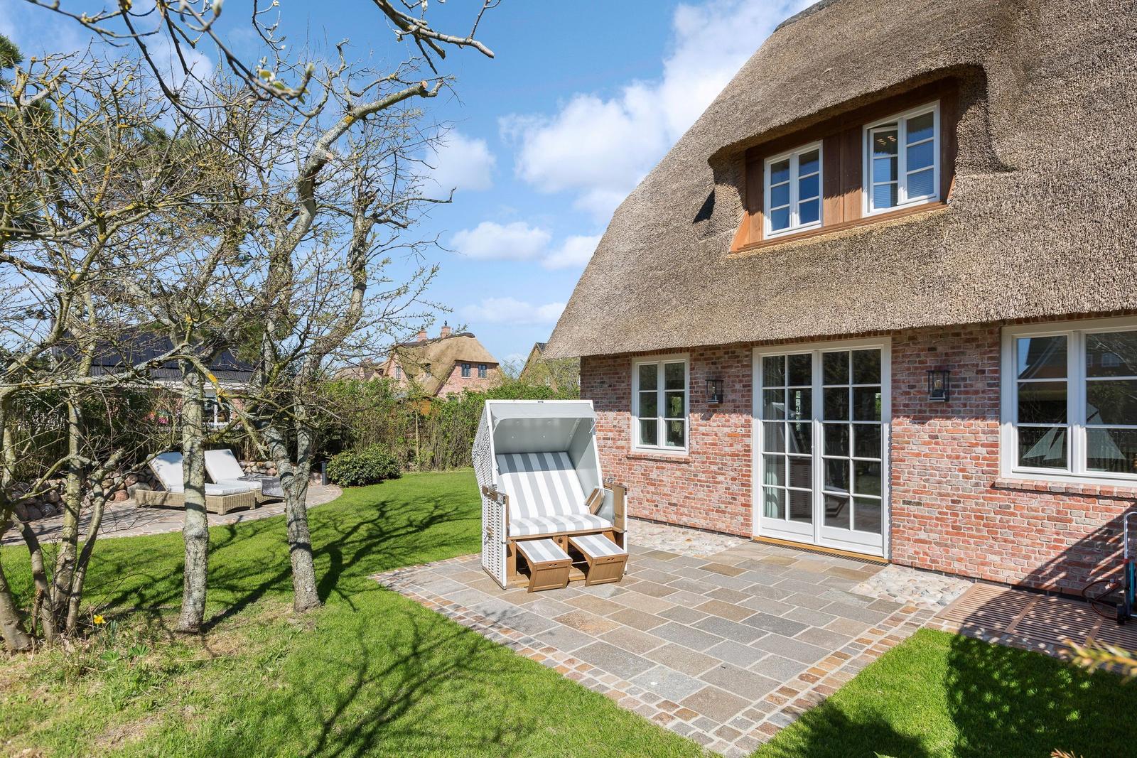Haus mit Strohdach, Terrasse und Strandkorb im Garten.