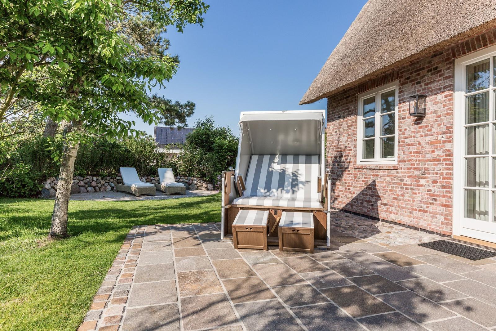 Haus mit Strohdach, Terrasse und Strandkorb im Garten.