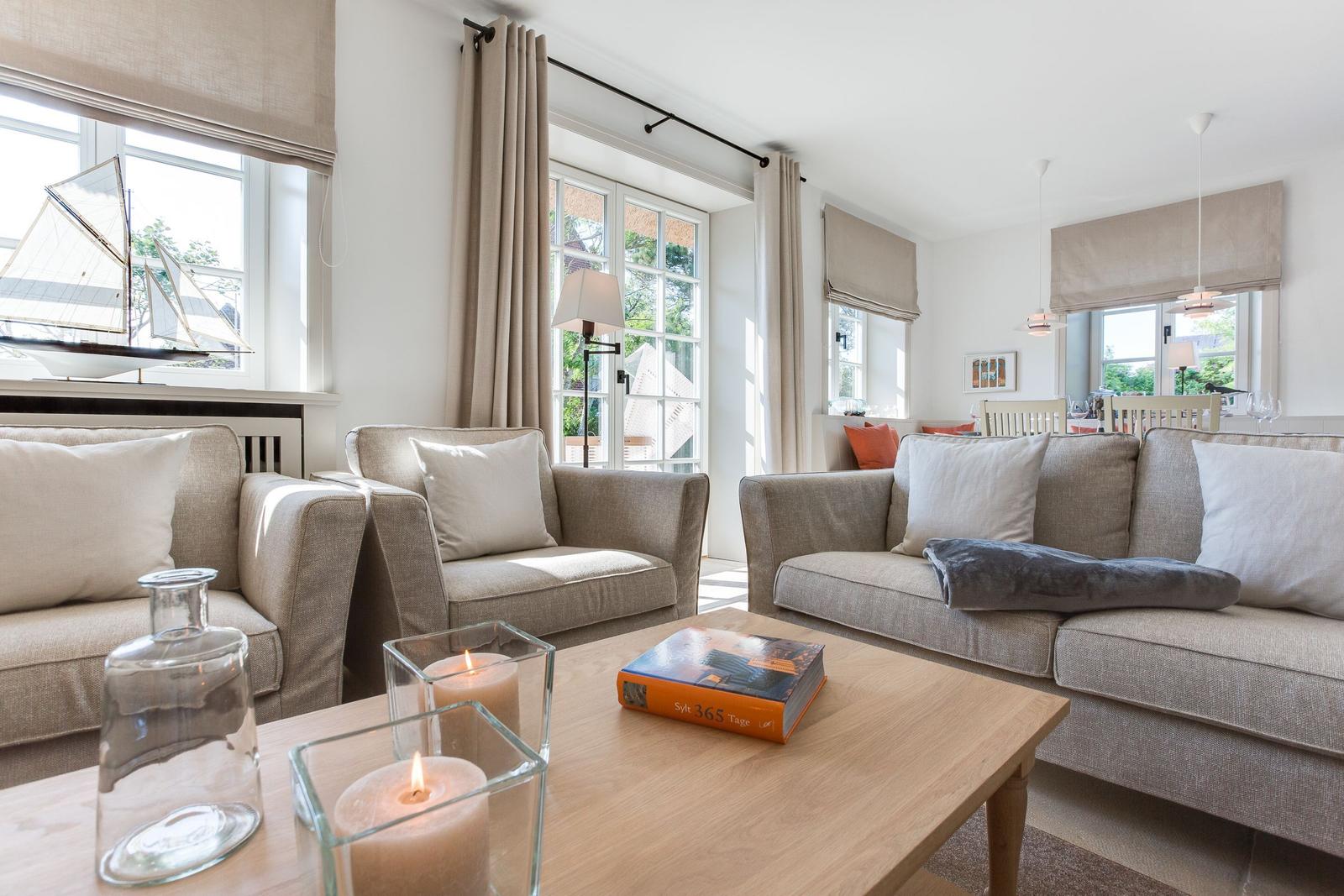 Wohnzimmer mit Sofa, Sessel und Tisch mit Kerzen und Buch.