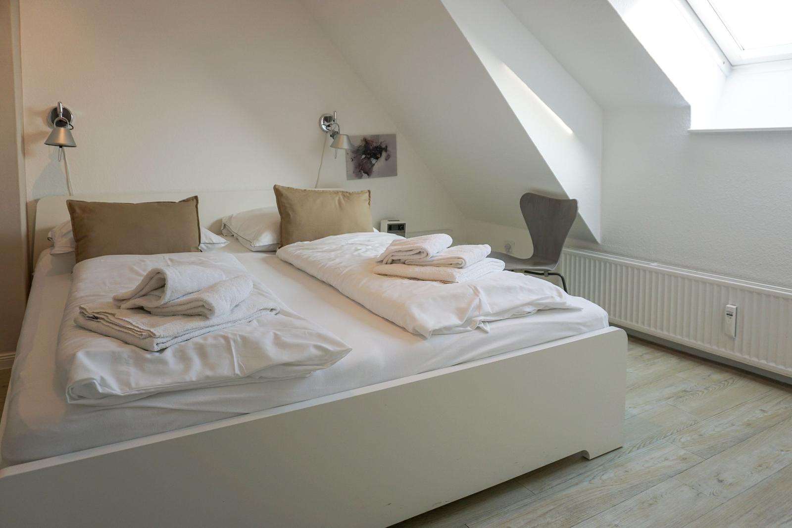 Bedroom with sloped ceiling, bed, chair, and skylight.