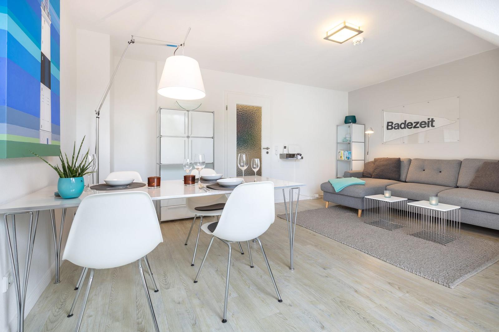 Living and dining area with gray sofa, white table set, and wooden floor.