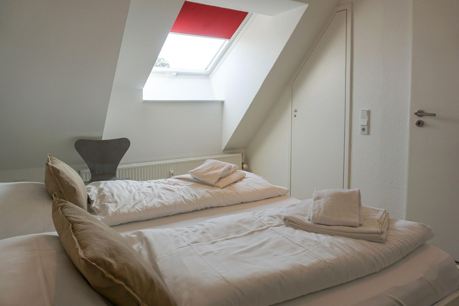 Attic room with sloped ceiling, double bed, and skylight with red blind.