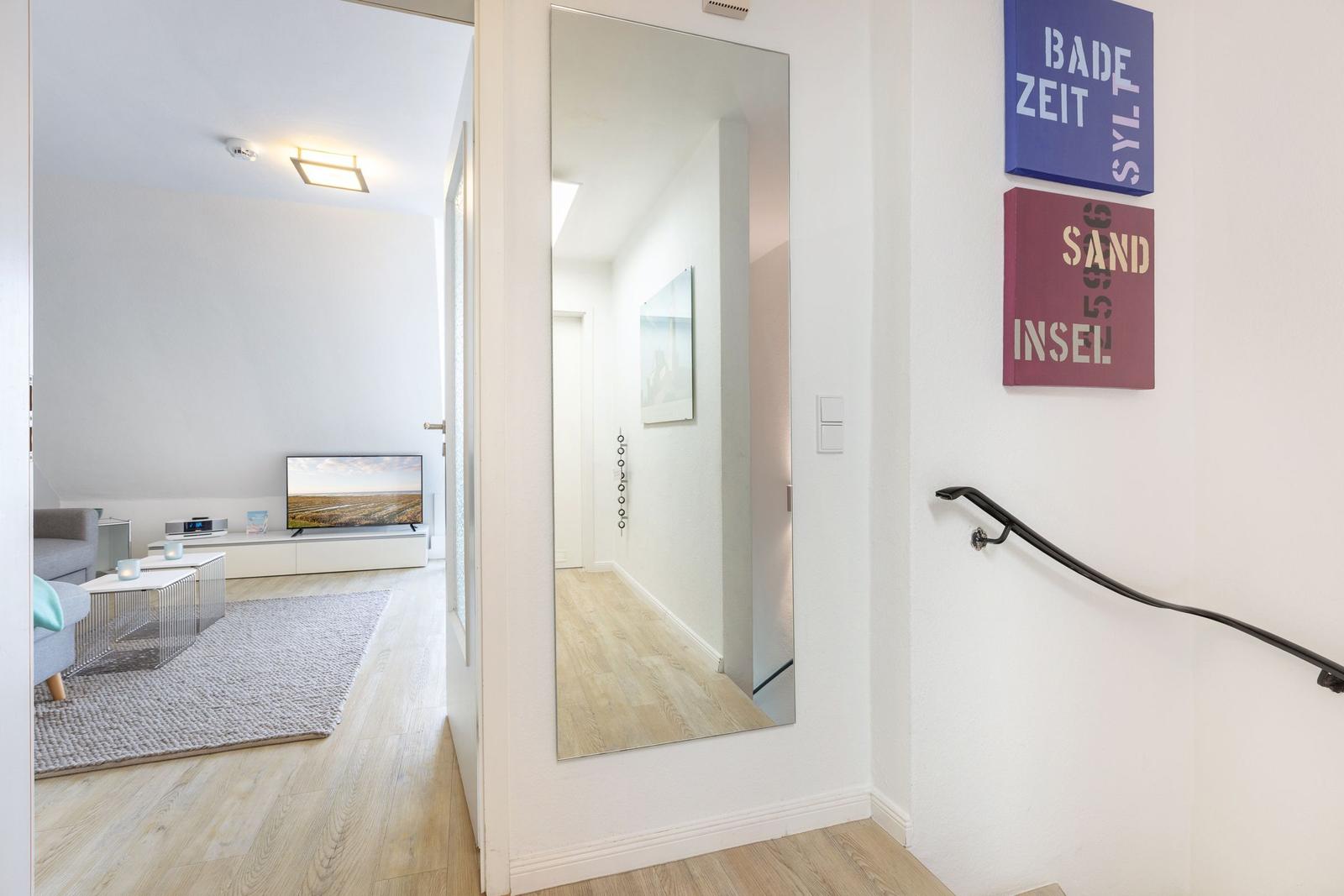 Entrance with mirror and wall art. View into living room with TV.