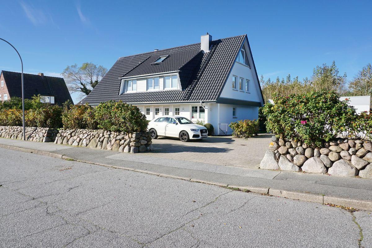 A white house with a black roof and paved yard. A car is parked in front of the house.