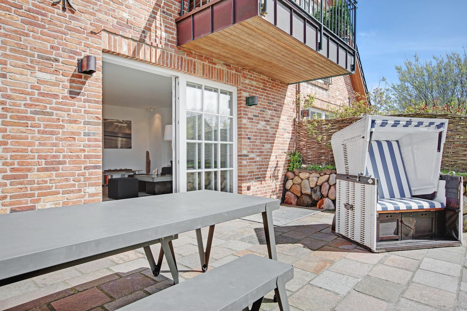 Terrasse mit Tisch, Bänken und Strandkorb vor Backsteinhaus