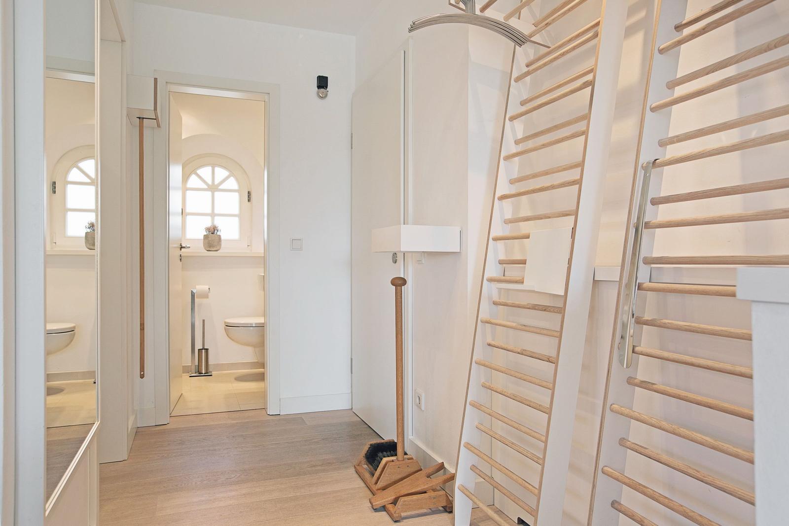 Flur mit Holzdielen, Bad mit Toilette und Fenster, Holzregale an der Wand.