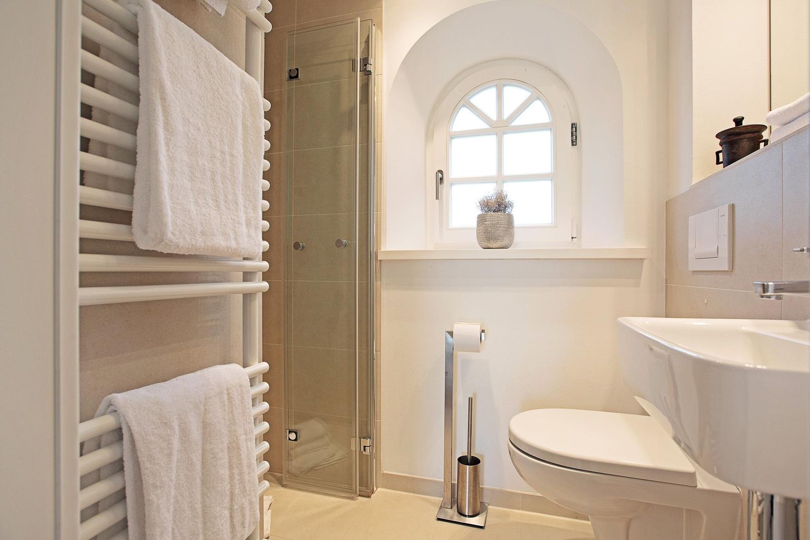 Badezimmer mit Dusche, Toilette, Waschbecken und Heizkörper mit Handtüchern.