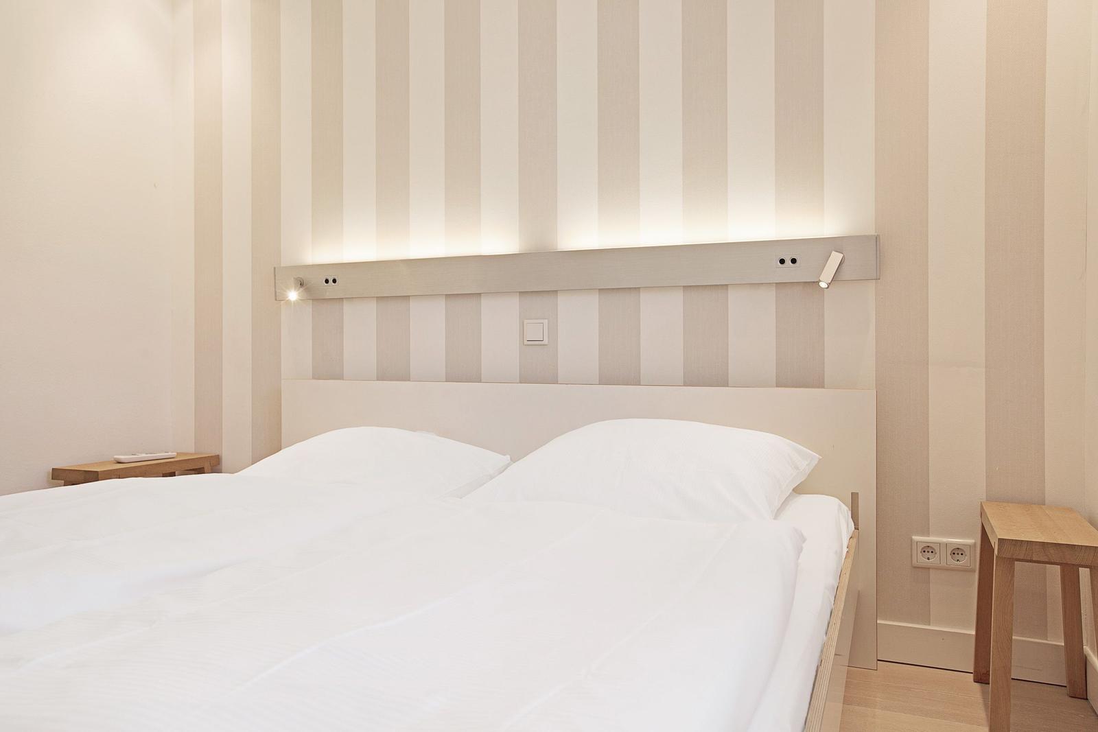 Schlafzimmer mit Bett, Nachttisch und gestreifter Wand