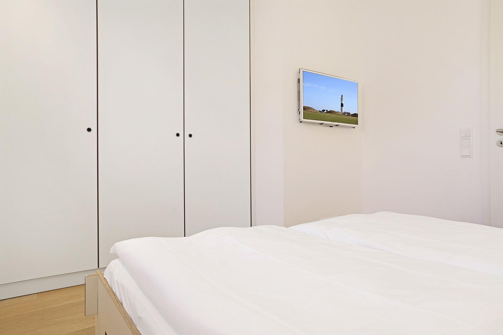 Schlafzimmer mit weißem Bett, Kleiderschrank und Wandbild