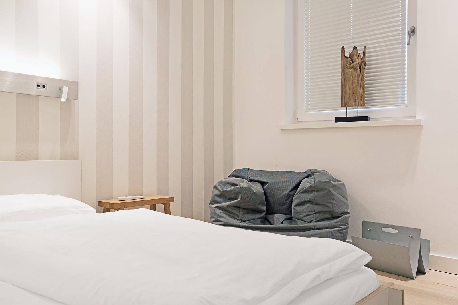 Schlafzimmer mit Bett, Fenster und Sitzgelegenheit.