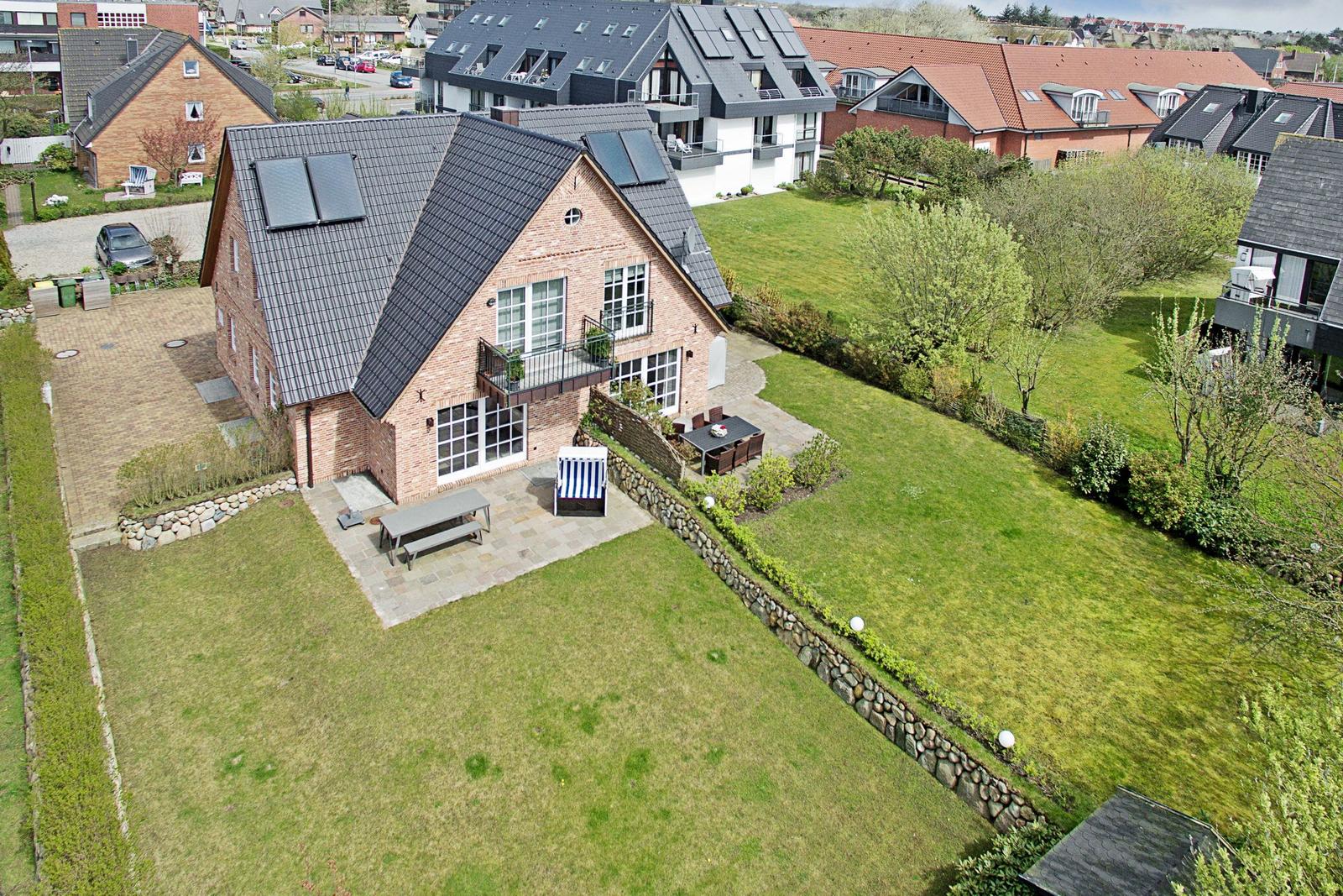 Haus mit Garten, Terrasse und Solaranlage. Umgeben von Grünflächen und Nachbarhäusern.