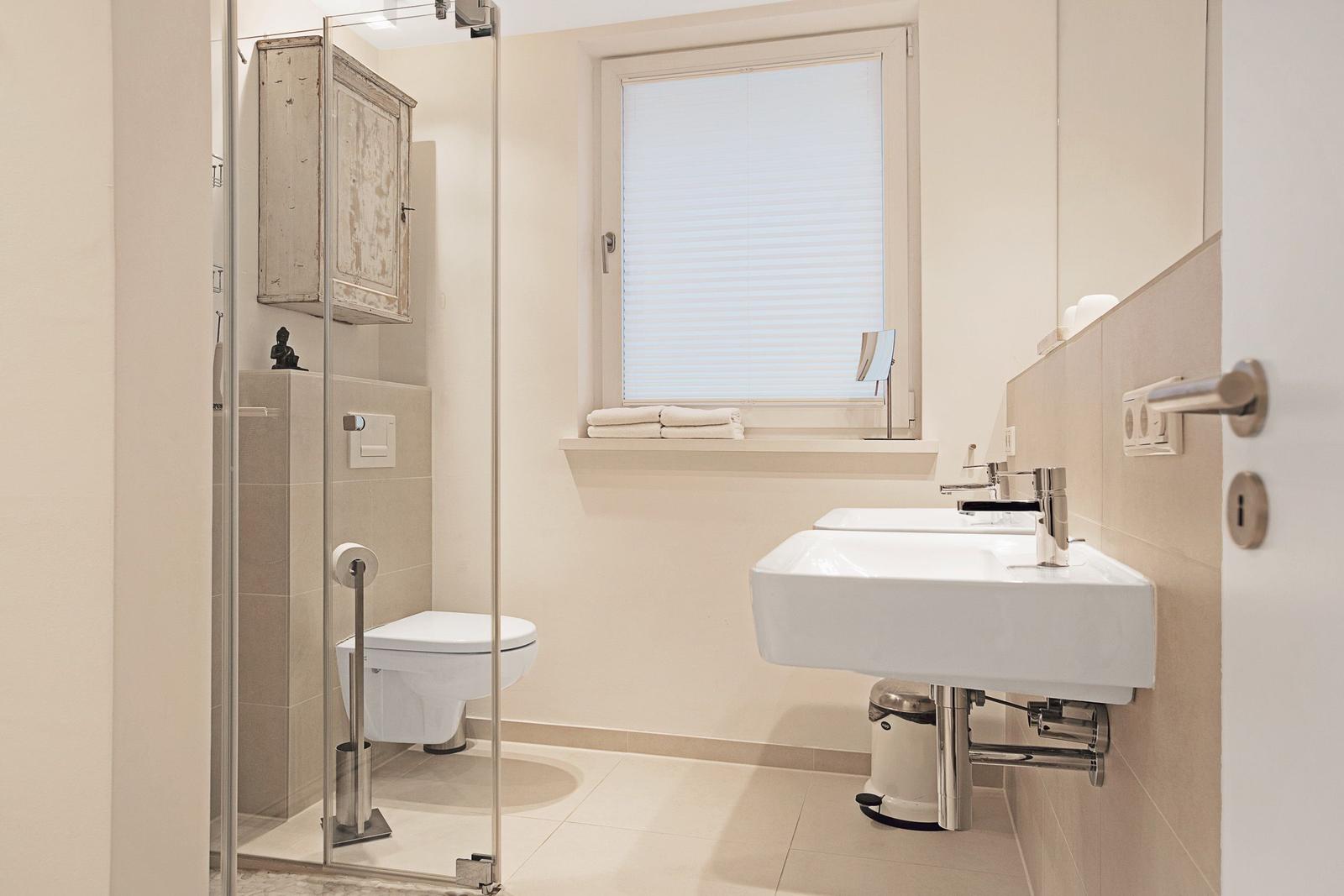 Badezimmer mit Dusche, Toilette, Waschbecken und Fenster.