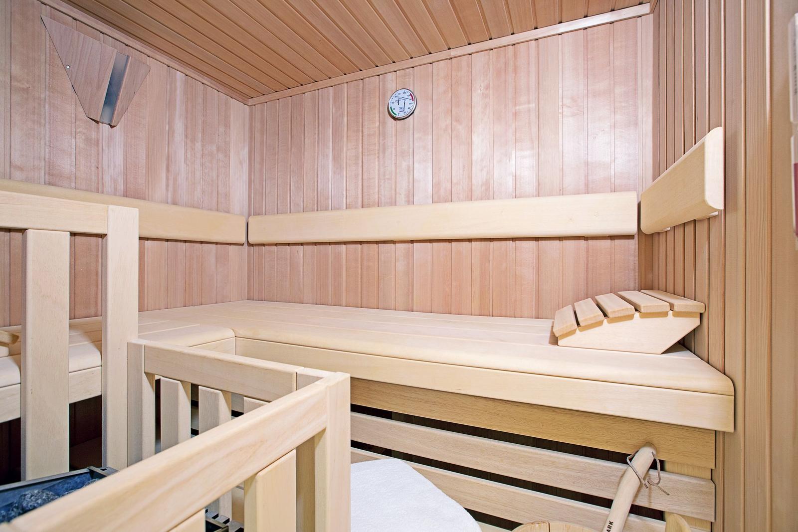 Holzsauna mit Sitzbänken und Thermometer an der Wand.