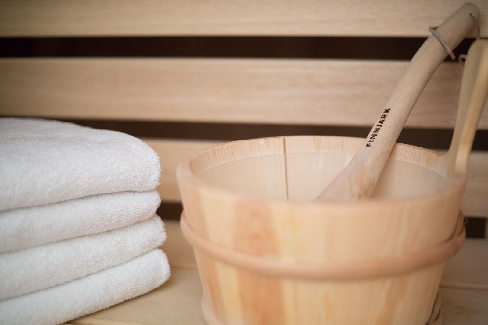 Holzschale mit Löffel und gestapelten Handtüchern in Sauna