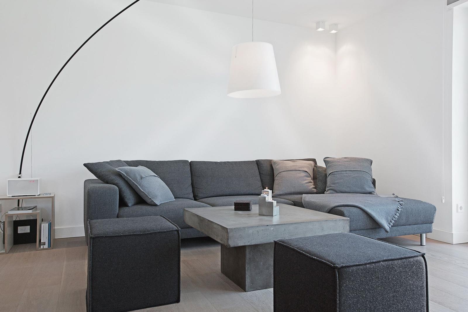 Ein Wohnzimmer mit grauem Sofa, Beton-Tisch und schwarzer Bogenlampe.