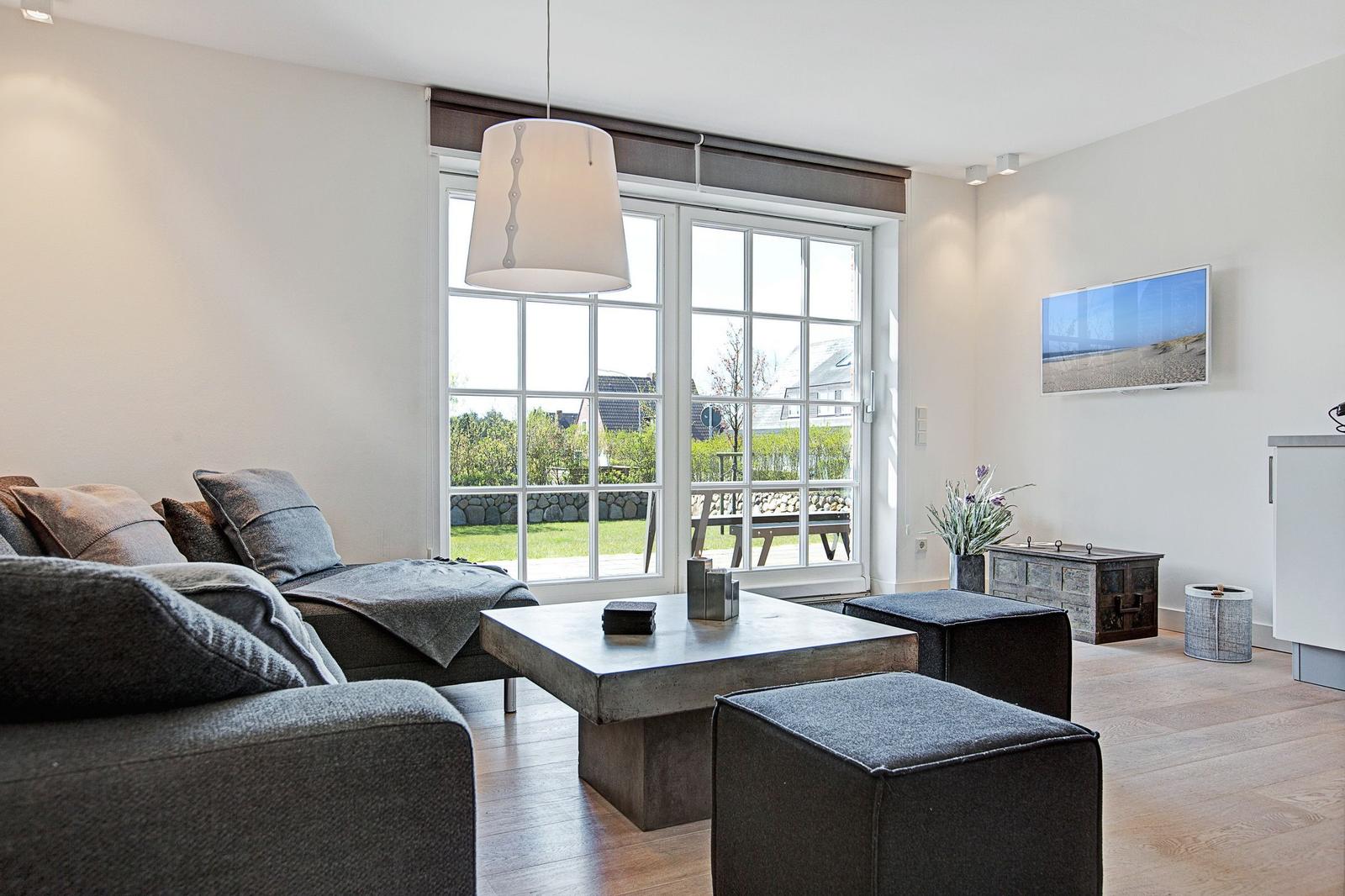 Wohnzimmer mit Sofa, Tisch und Fenster zur Außenterrasse.