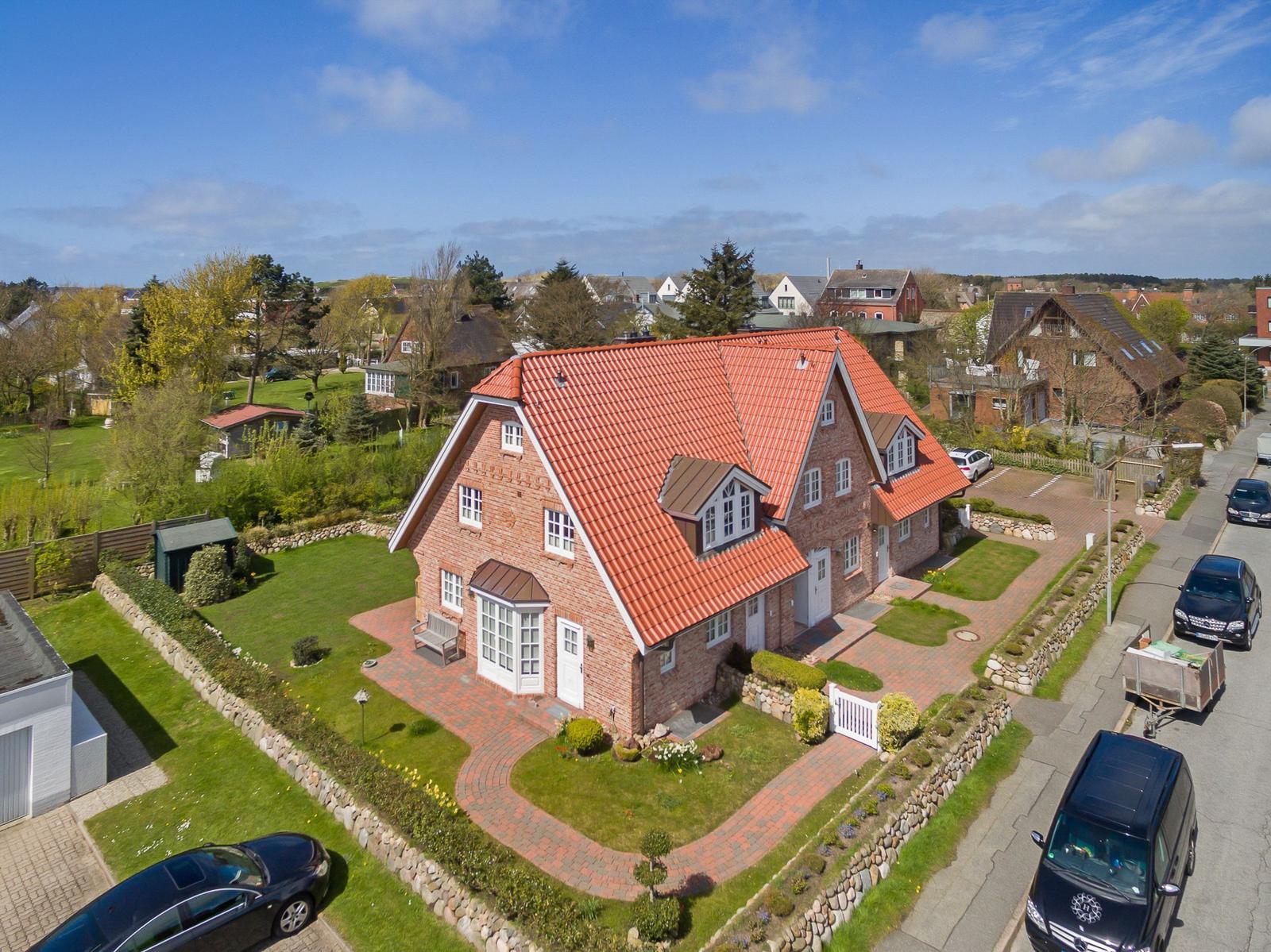 Ein Haus mit rotem Dach und gepflastertem Hof. Umgeben von Grünflächen und Bäumen.