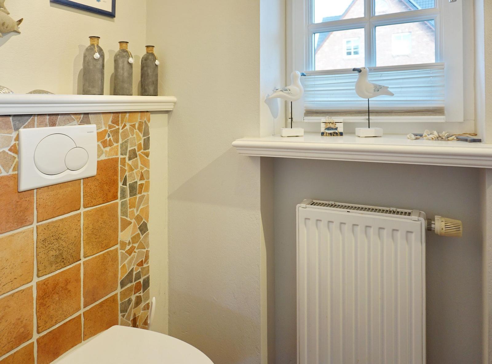 Toilette mit Mosaikwand, Fenster mit Vogeldekoration und Heizkörper.