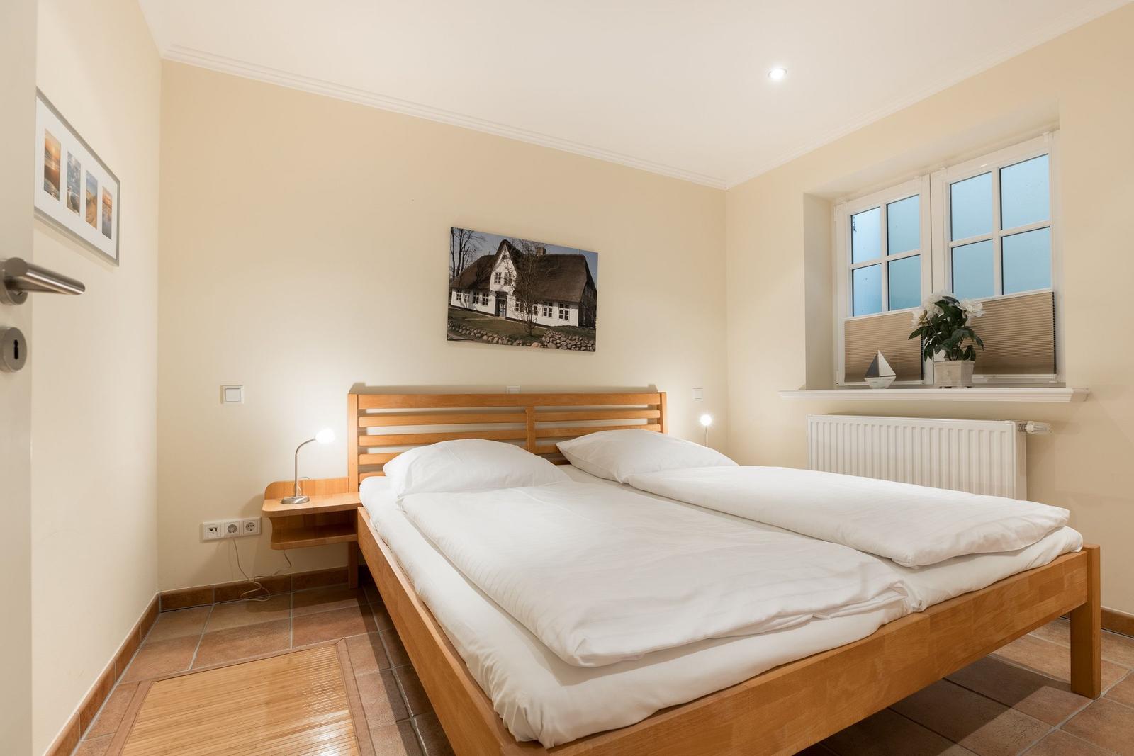 Schlafzimmer mit Doppelbett, Holzrahmen, Fenster und Wandbild.