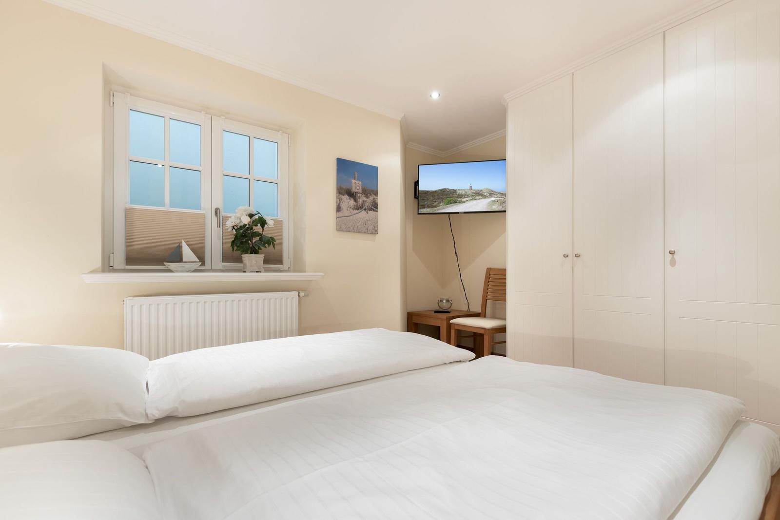 Schlafzimmer mit Doppelbett, Fenster, Kleiderschrank und Wand-TV.