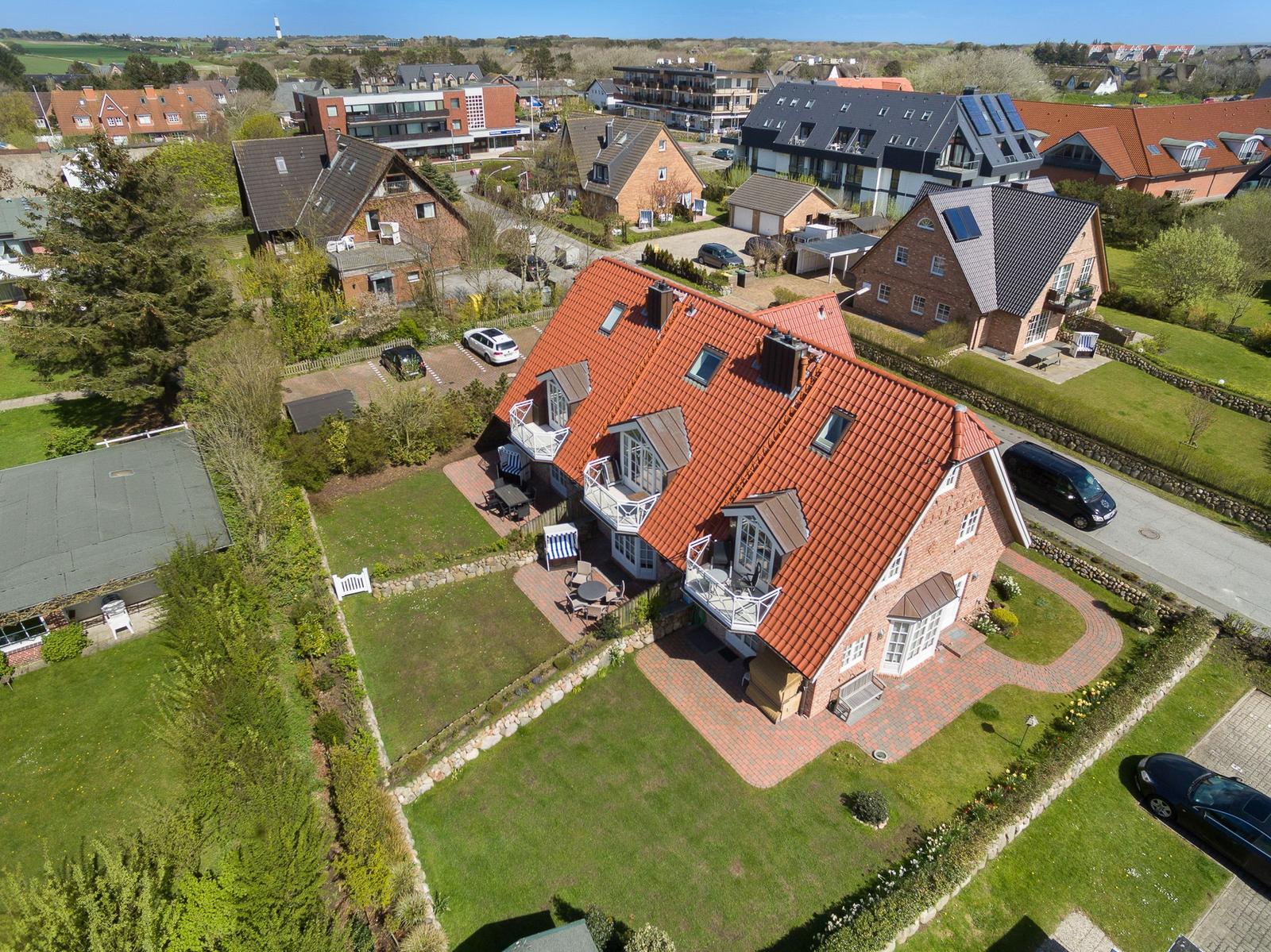 Haus mit rotem Dach und Garten. Mehrere Balkone und Parkplätze sichtbar.