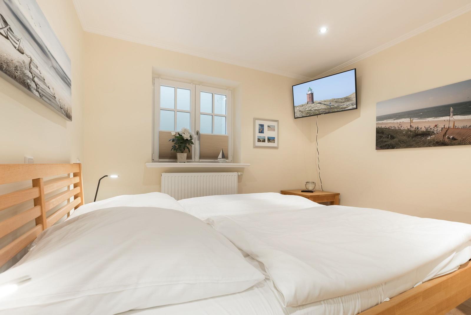 Schlafzimmer mit Doppelbett, Fenster, Fernseher und Wandbildern.
