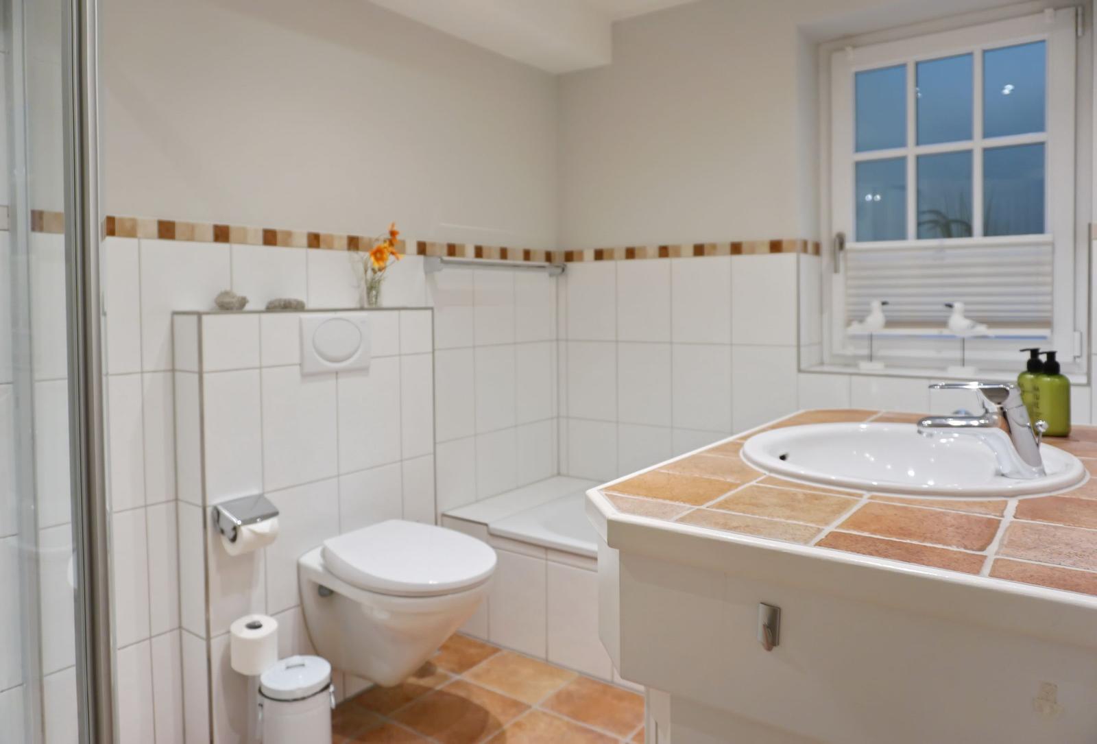 Badezimmer mit Toilette, Waschbecken und Dusche. Fenster mit Jalousie.