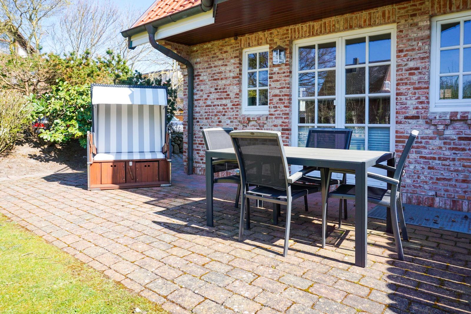 Terrasse mit Tisch, Stühlen und Strandkorb vor Backsteinhaus
