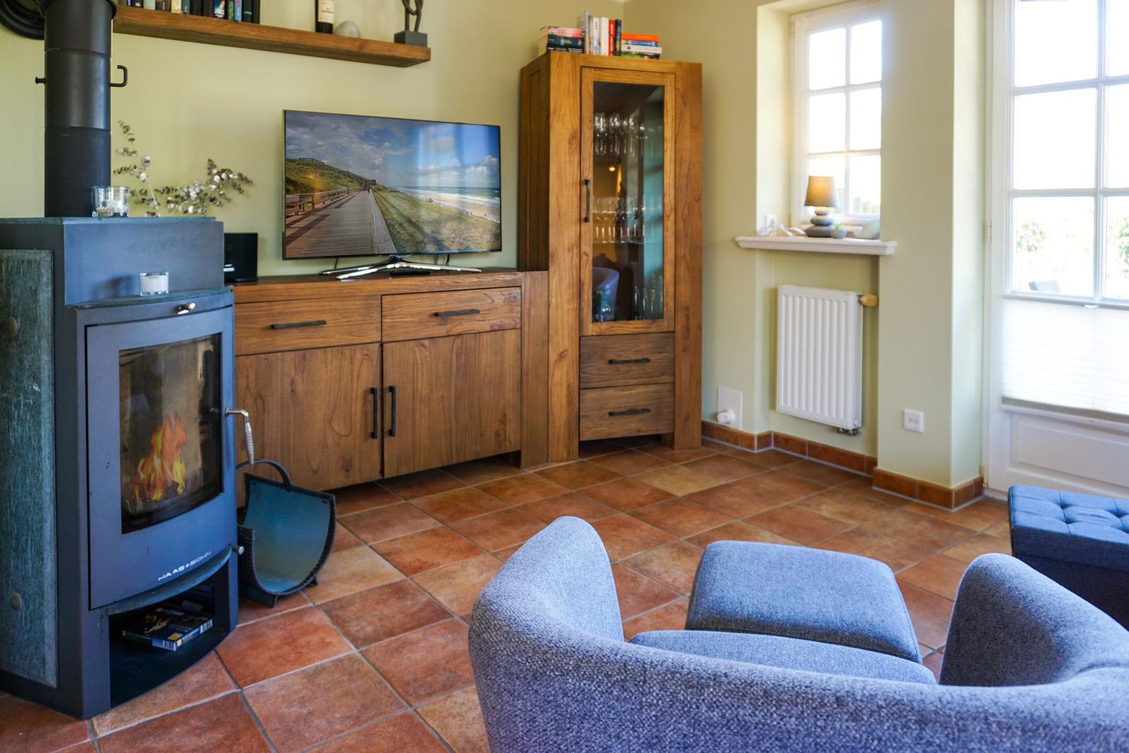 Wohnzimmer mit Kamin, Fernseher und Holzmöbeln auf Terrakottboden.